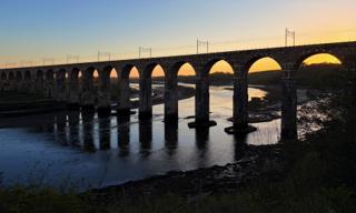 A bridge over a river with its arches set against a sunset.