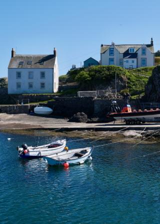 A serene coastal scene with boats moored to the shore by an idyllic body of water under a clear sky.