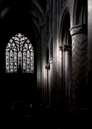 A gothic cathedral with stained glass windows with columns illuminated by sunlight.