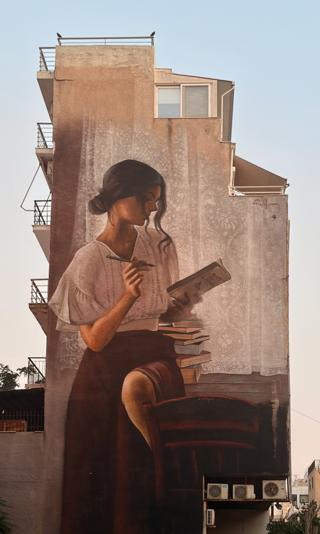 A mural of a woman reading a book painted on the side of a building.