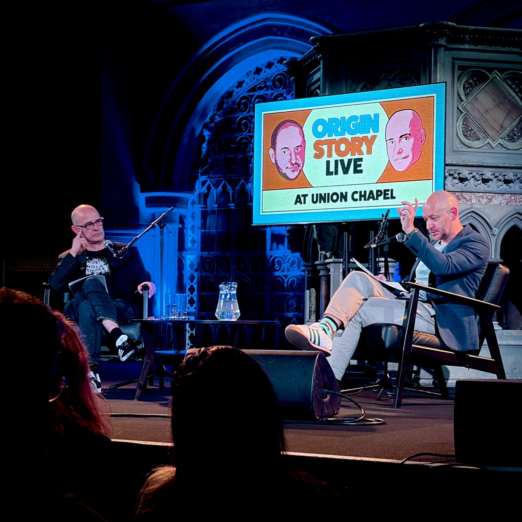 Dorian Lynskey and Ian Dunt sat on chairs behind microphones in a gothic setting.